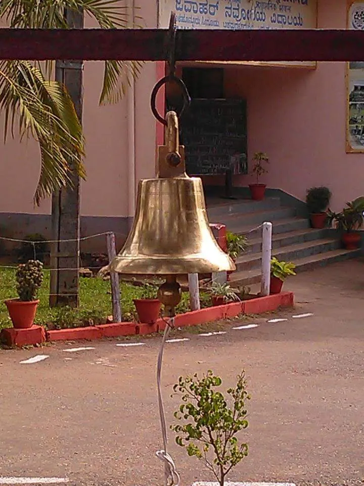 A brass bell hanging from a bar in front of a school building.