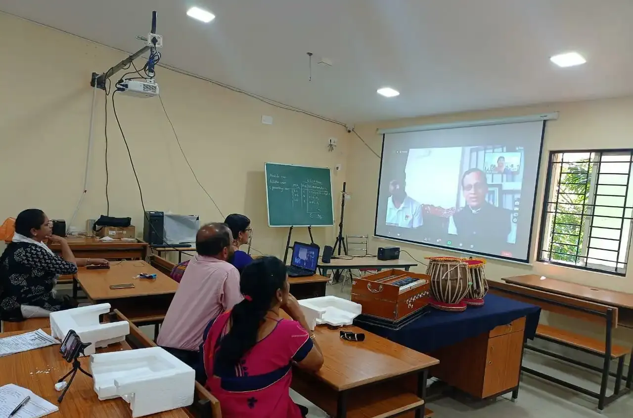 People seated at desks facing a projector screen showing a video call.